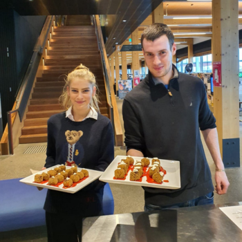Two people smiling and holding plates of food in a modern indoor setting.